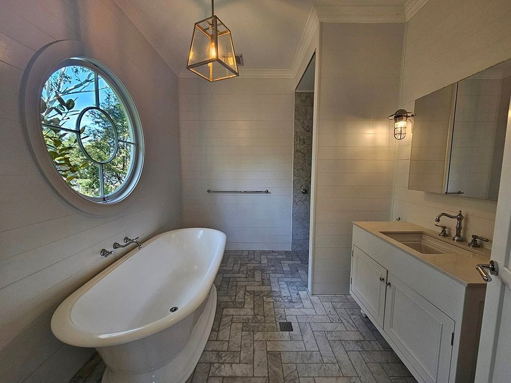 A Clean White Bathroom With Bathtub, Round Window And Cabinets — A Perfect Move And Clean In Welby NSW
