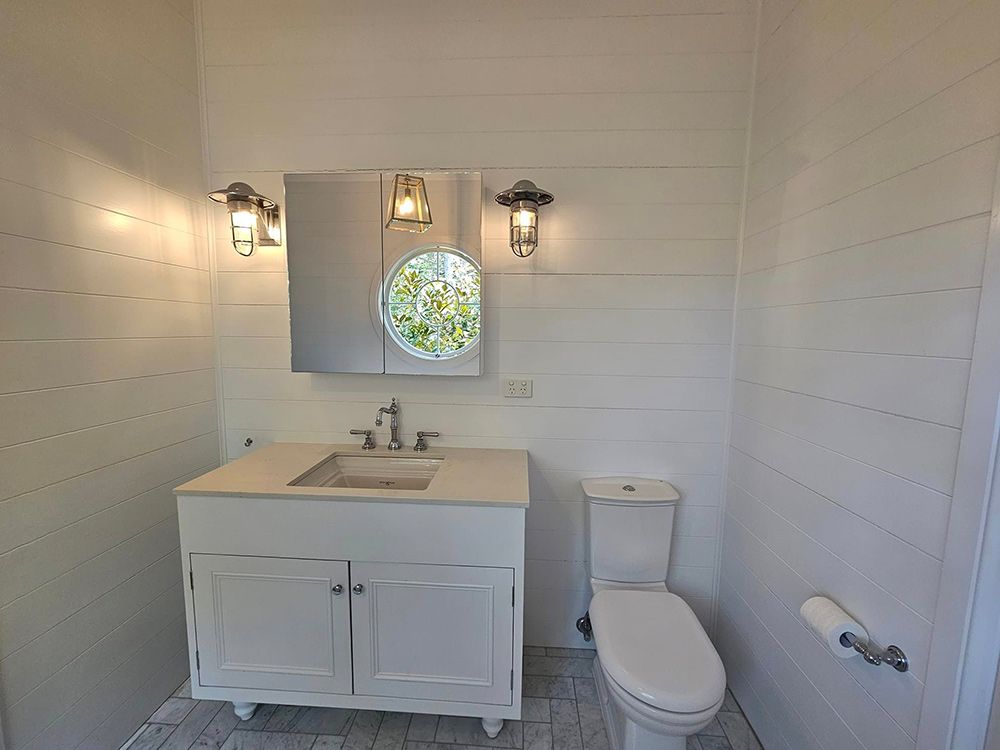 Bathroom with White Cabinet, Toilet Seat and Sink with Mirror having Two Lamps either side on the Wall— A Perfect Move And Clean In Moss Vale NSW