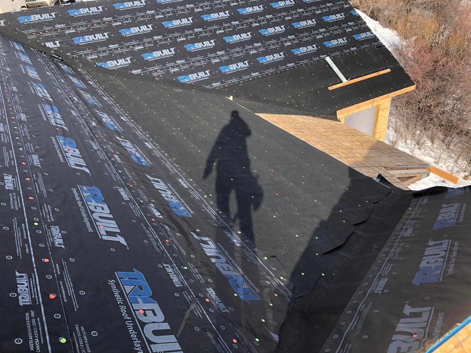 A shadow of a person is cast on a piece of roofing material