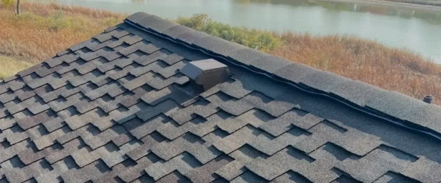A close up of a roof with shingles on it and a river in the background.