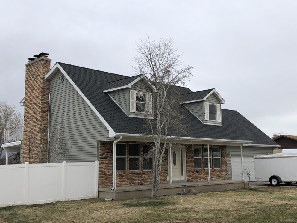 A house with a black roof and a white fence in front of it.