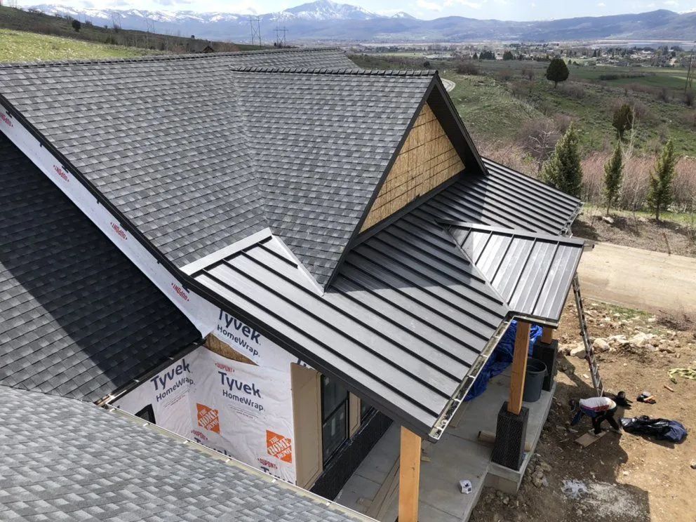 Newly built house with dark gray roofs, siding, and metal roofing; blue sky.