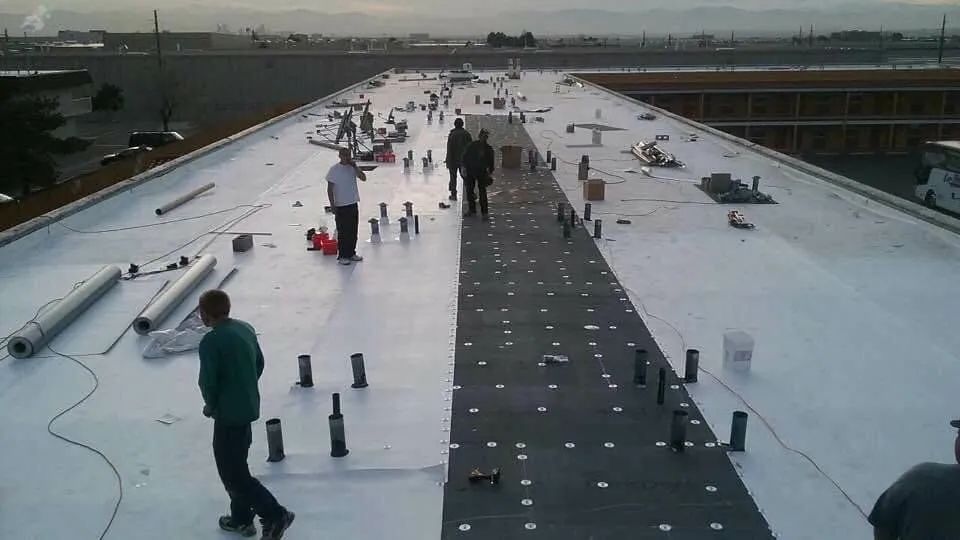 Construction workers on a flat roof installing roofing material.  Workers stand near rolls of material.