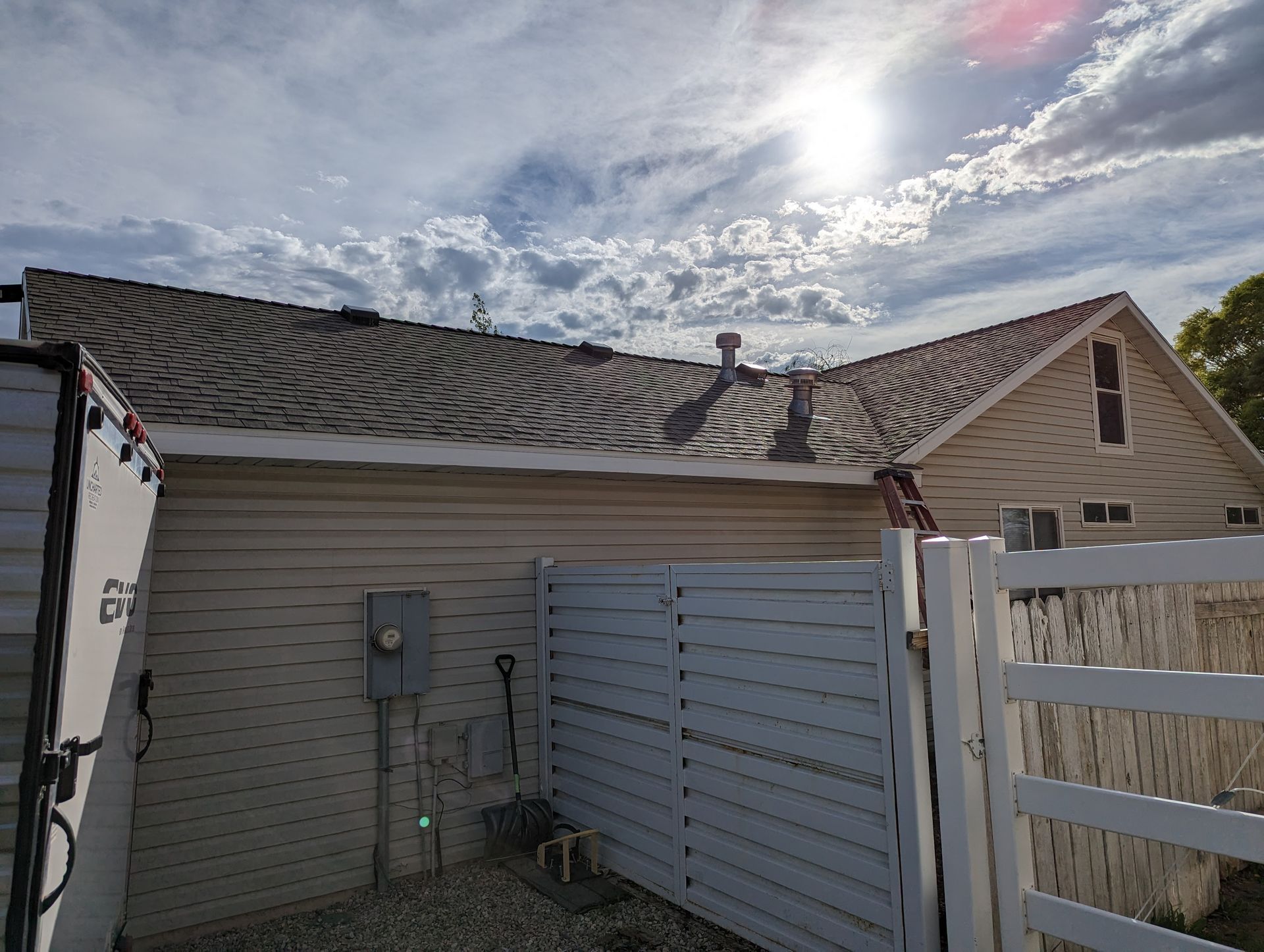 A white trailer is parked in front of a house with a roof.