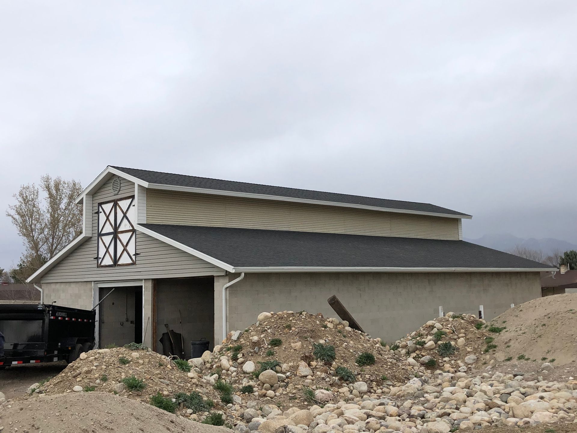 A barn with a black roof is sitting next to a pile of rocks.