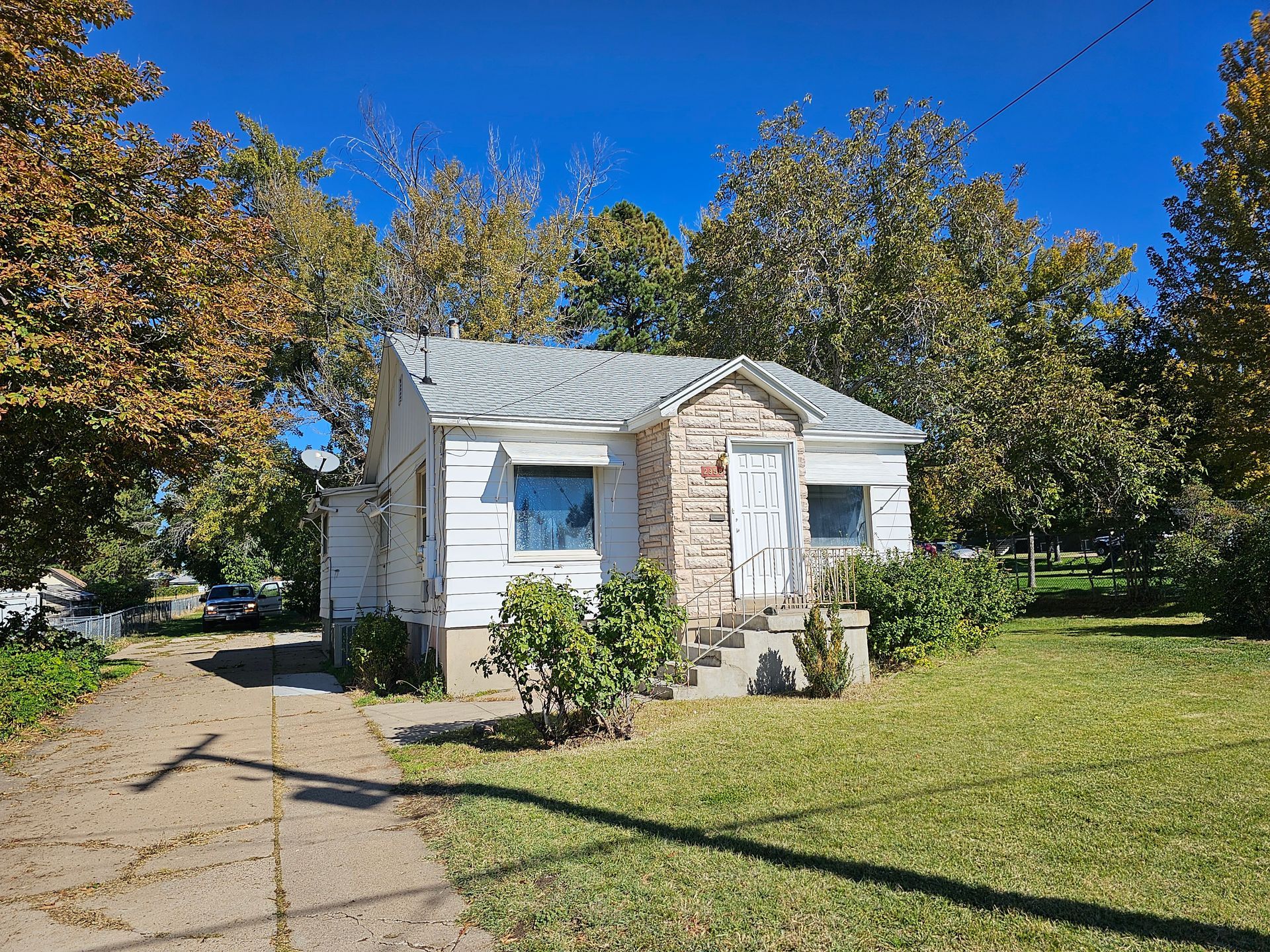 A small white house is surrounded by trees and grass on a sunny day.