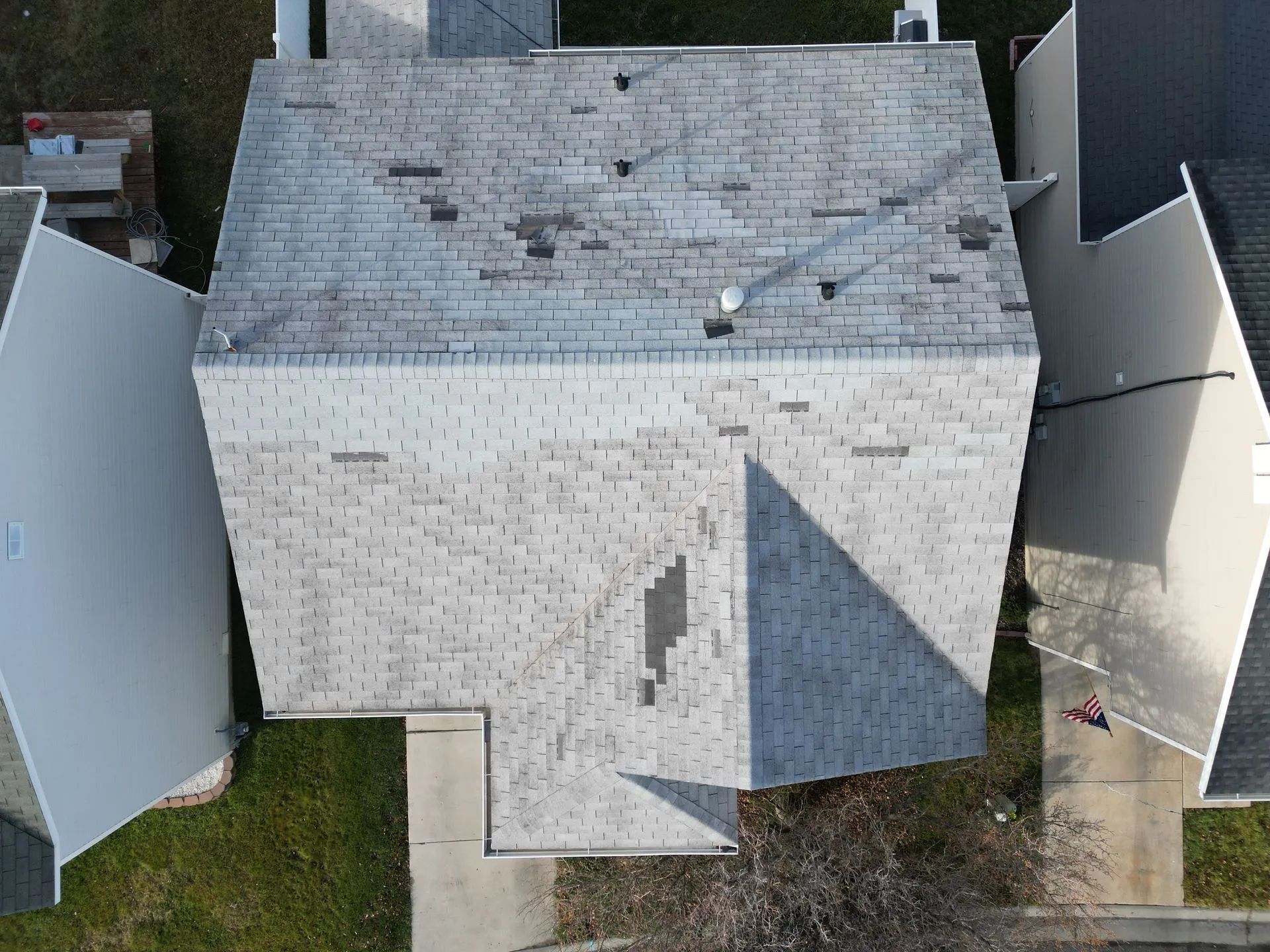 An aerial view of a gray, multi-pitched residential roof showing signs of wear, missing shingles, and patchy discoloration.