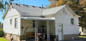 A small white house with a gray roof and a porch.