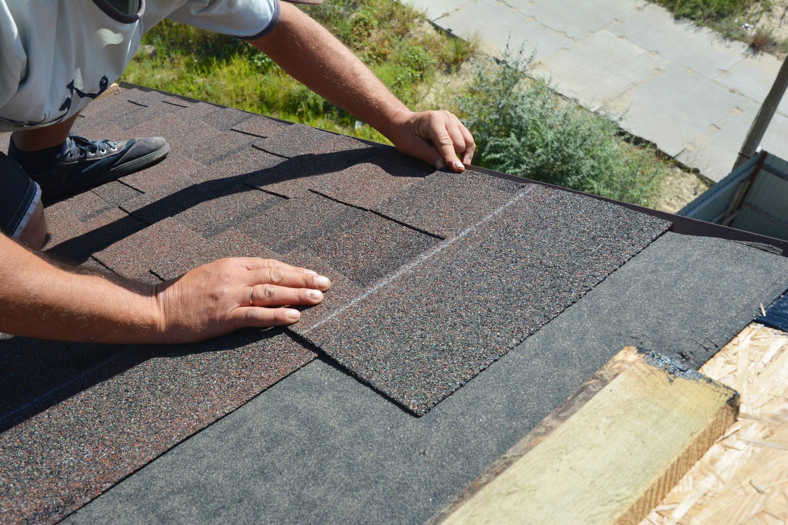 Worker installing brown asphalt shingles on a roof