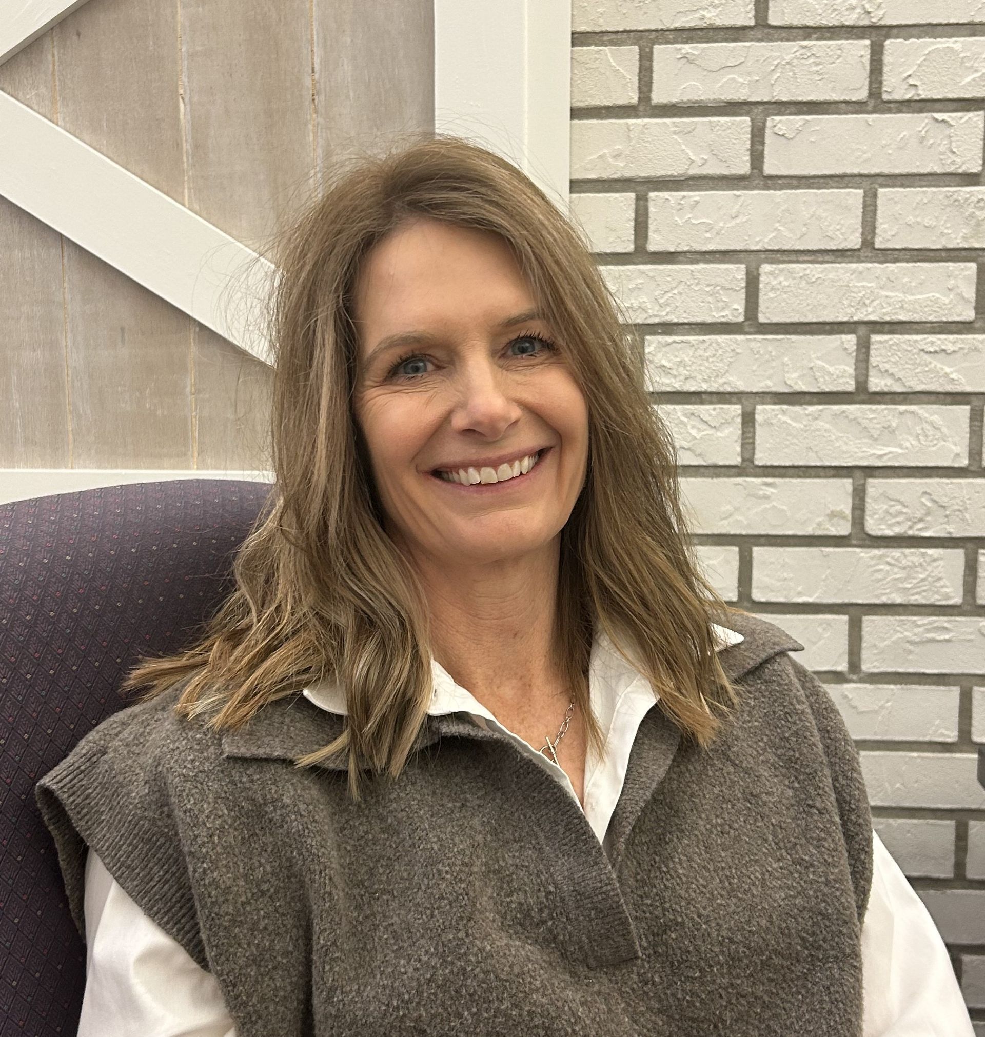 Woman with auburn hair and freckles looking at the camera, wearing a light tan coat, standing outside.