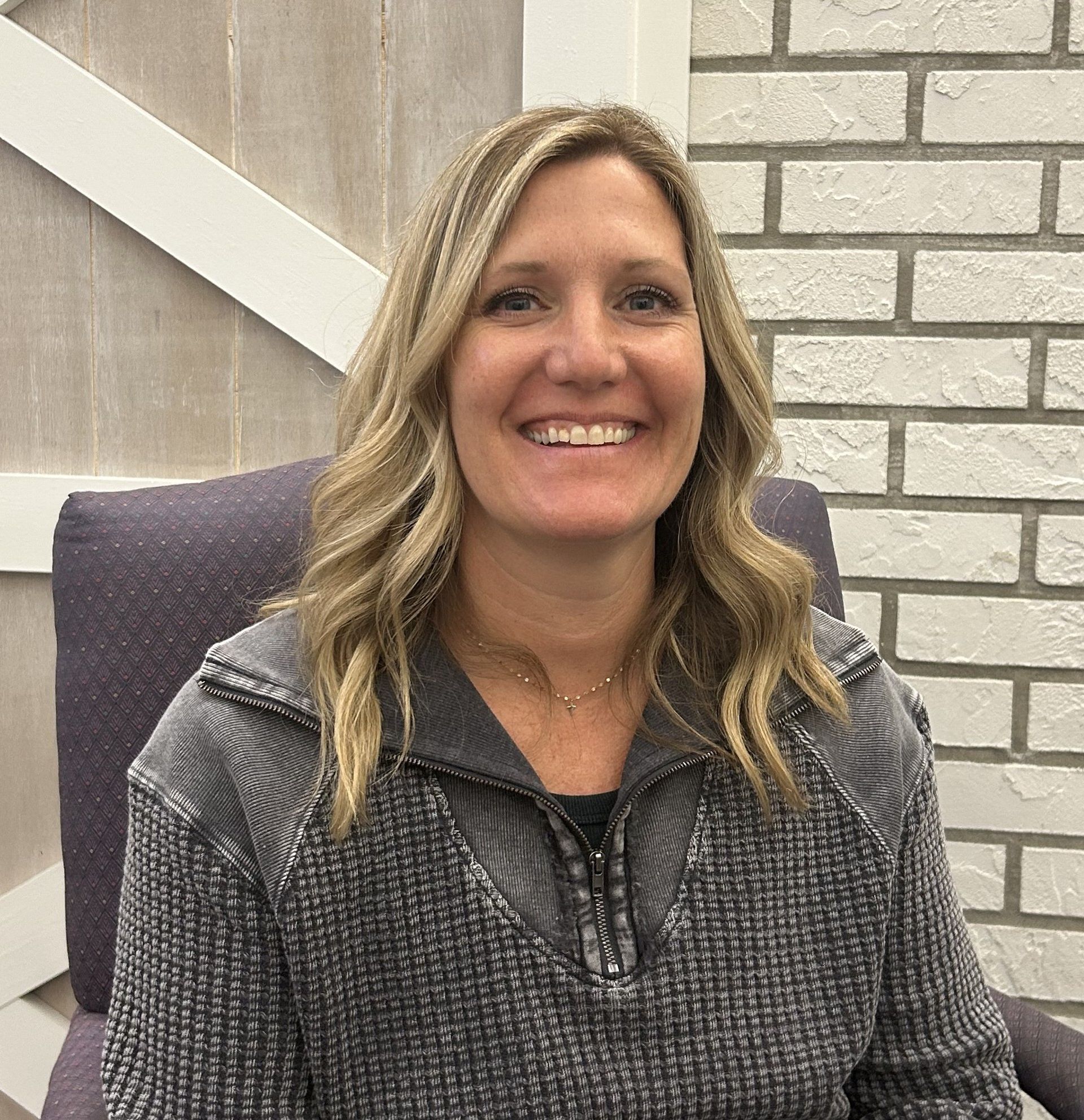 Man with light skin and light brown hair, looking at the camera. Black shirt and a dark background.