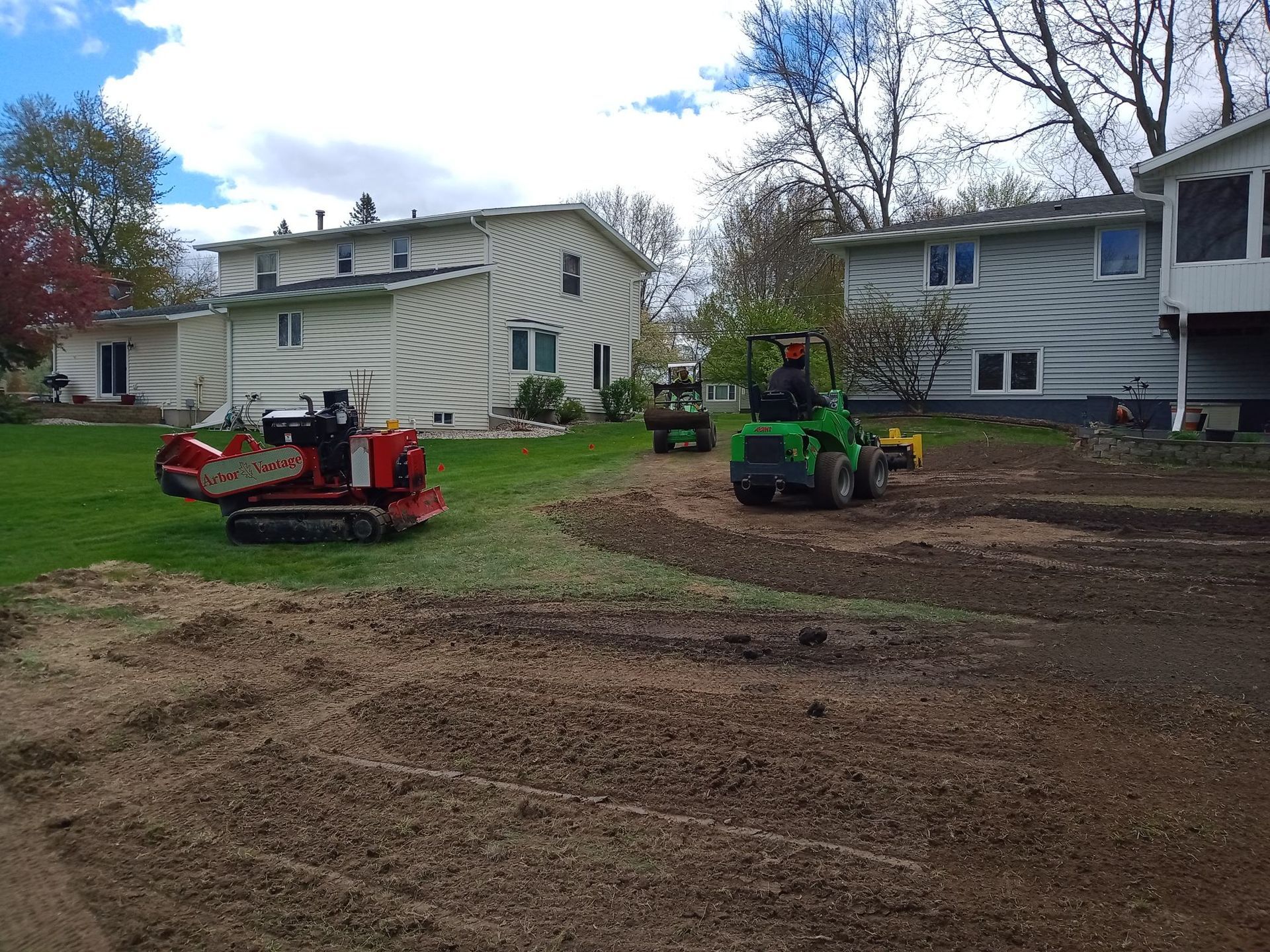 A tractor is driving down a dirt road in front of a house.