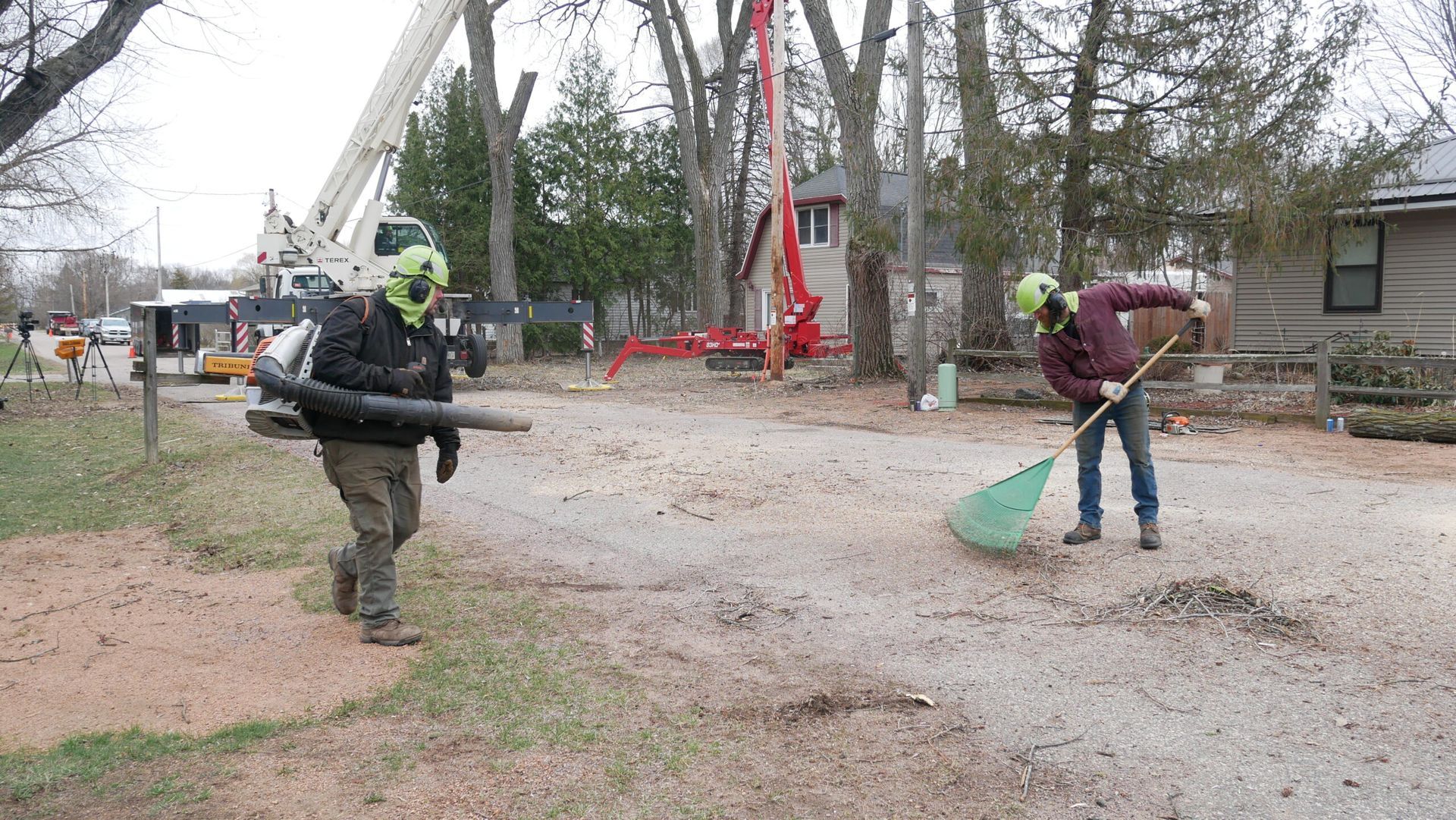 Two men are raking leaves in a driveway in front of a house.