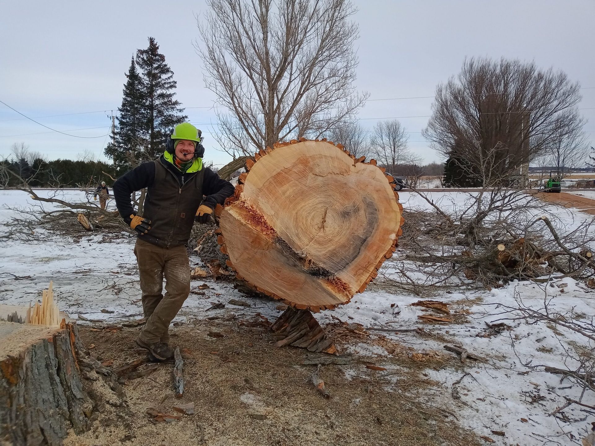 A man is standing next to a large tree stump in the snow.