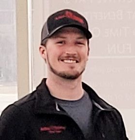 A man with a beard is wearing a baseball cap and smiling.