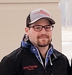 A man wearing a hat and glasses is standing in front of a wall.