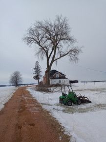 A green tractor is parked on the side of a snow covered road.