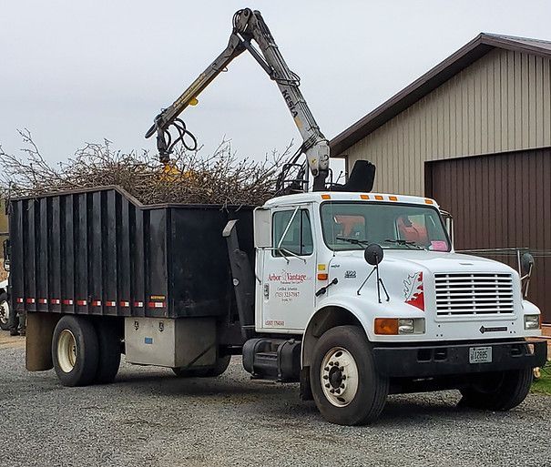 A white truck with a crane attached to it is loading branches into a dumpster.