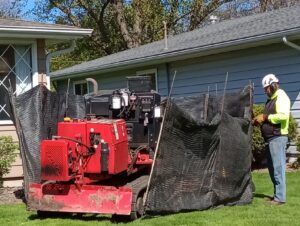 A man is standing next to a red machine in front of a house.