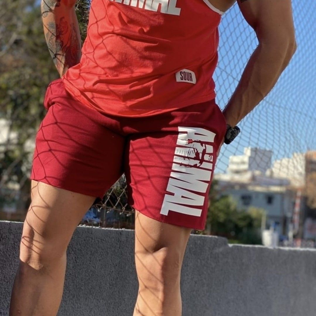 Un hombre con camiseta roja y pantalones cortos está afuera, con la mano en el bolsillo.