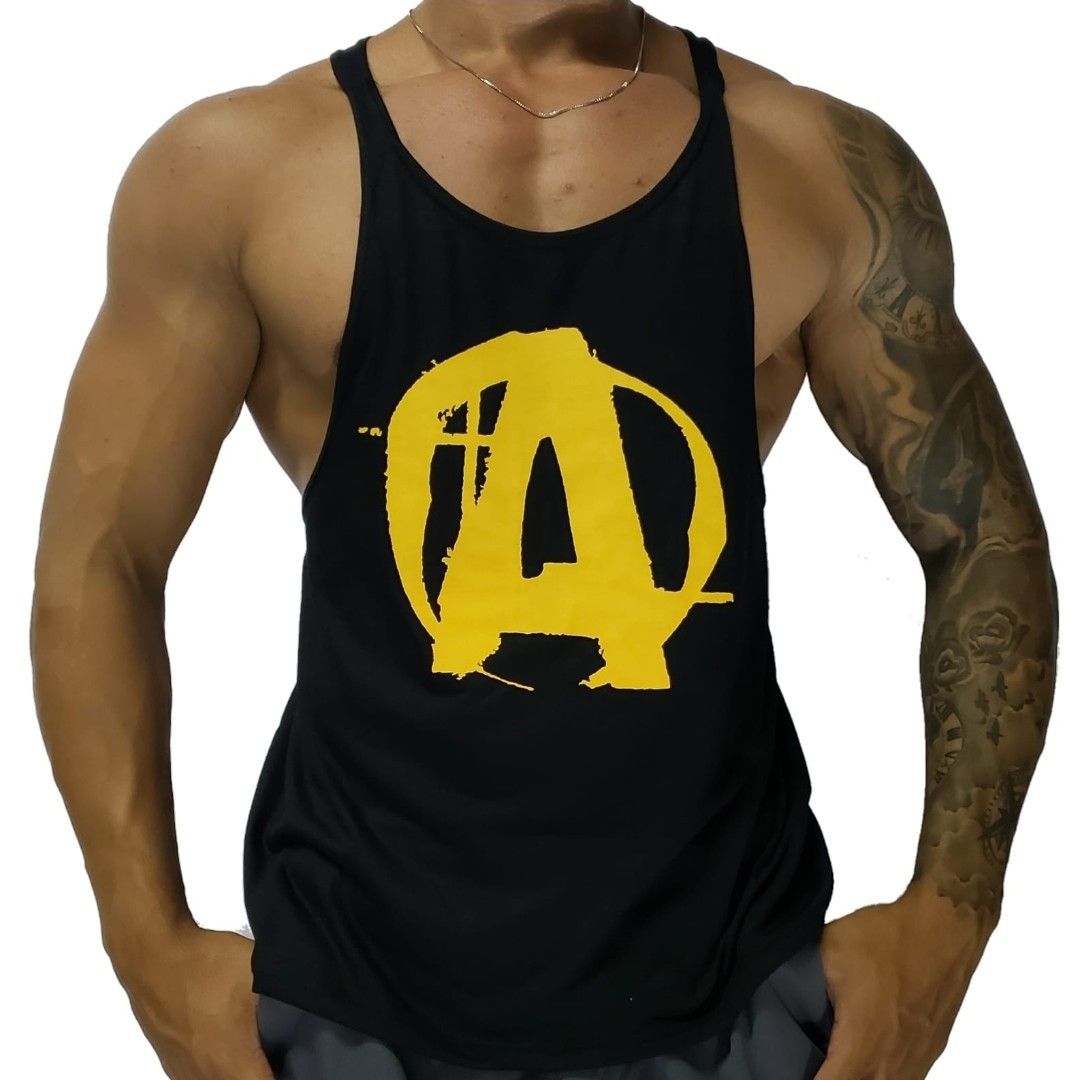 Hombre con una camiseta negra sin mangas con el logo "A" amarillo, brazos musculosos, collar y un tatuaje en todo el brazo.