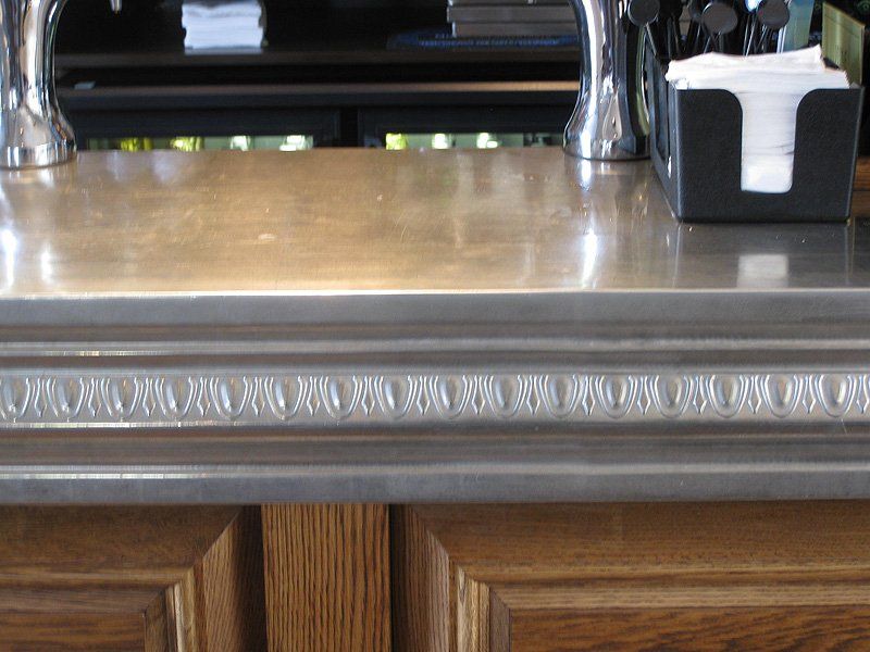 A bar with a stainless steel counter top and wooden cabinets