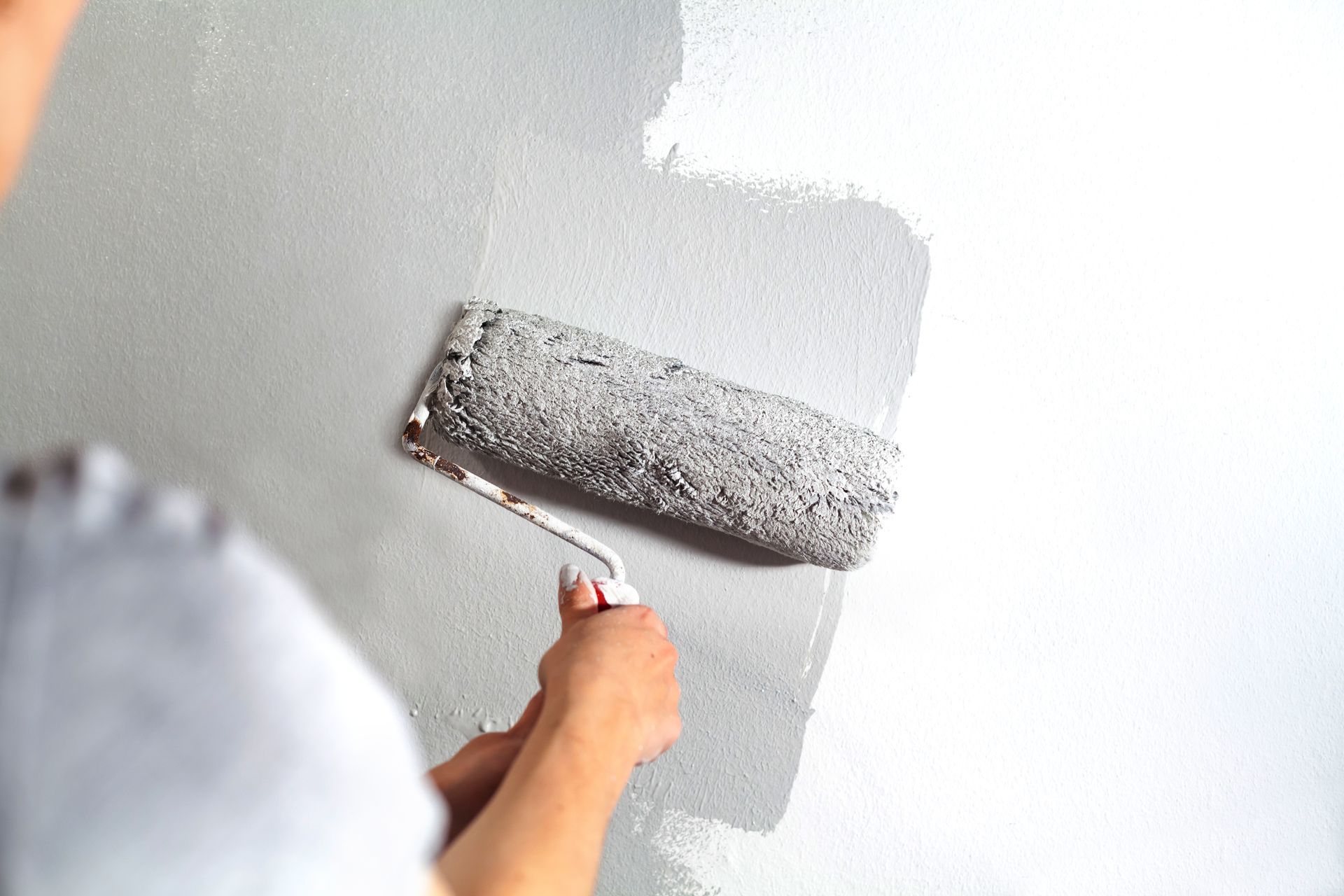 A person is painting a wall with a paint roller.