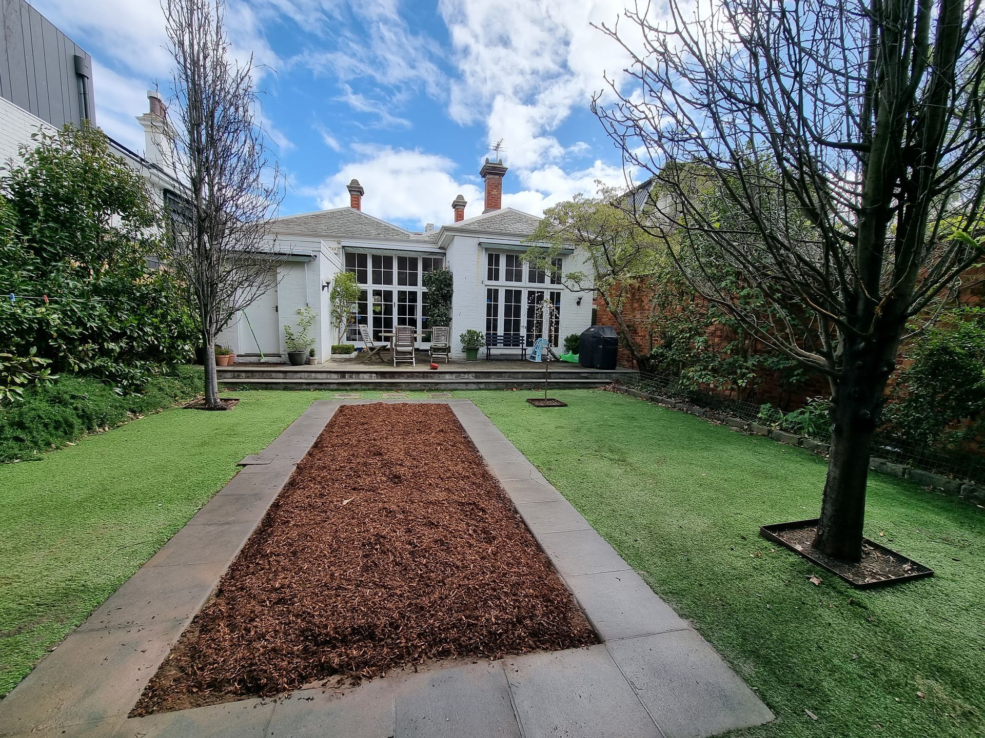 A rectangular garden features a central wood-mulch bed, surrounded by lawn, trees, and a house with a back porch and yard — All Over Pool Removals in Narre Warren South, VIC