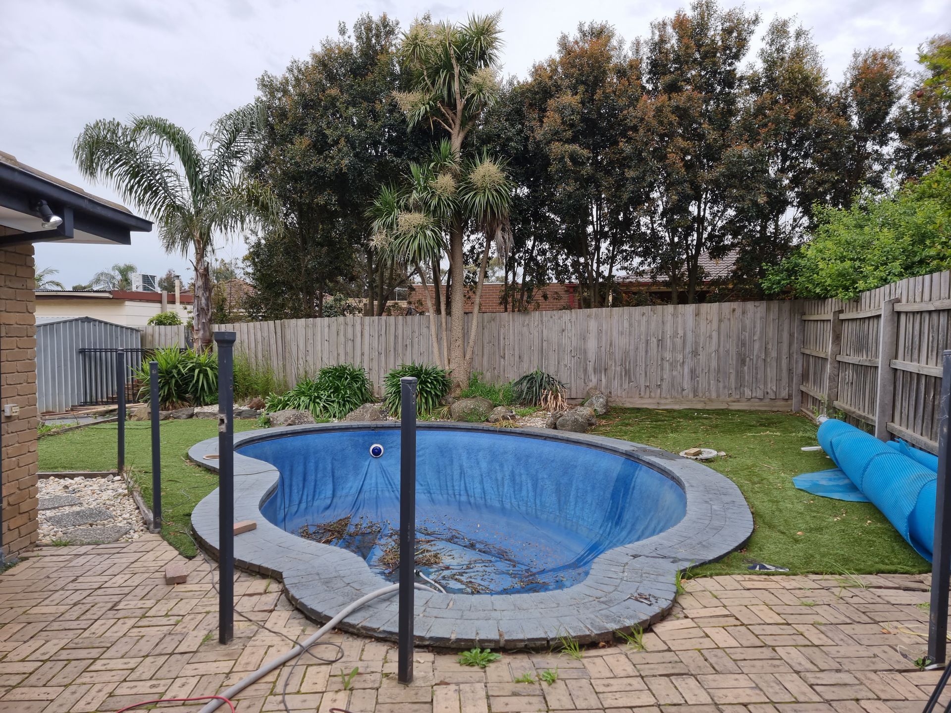 A small, blue-lined kidney-shaped swimming pool in a backyard with a brick patio and wooden fence — All Over Pool Removals in Doncaster, VIC