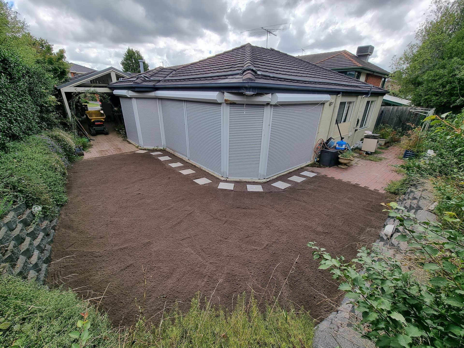 A landscaped backyard featuring a large patch of fresh soil, a stepping stone path, and a house with outdoor blinds — All Over Pool Removals in Narre Warren South, VIC