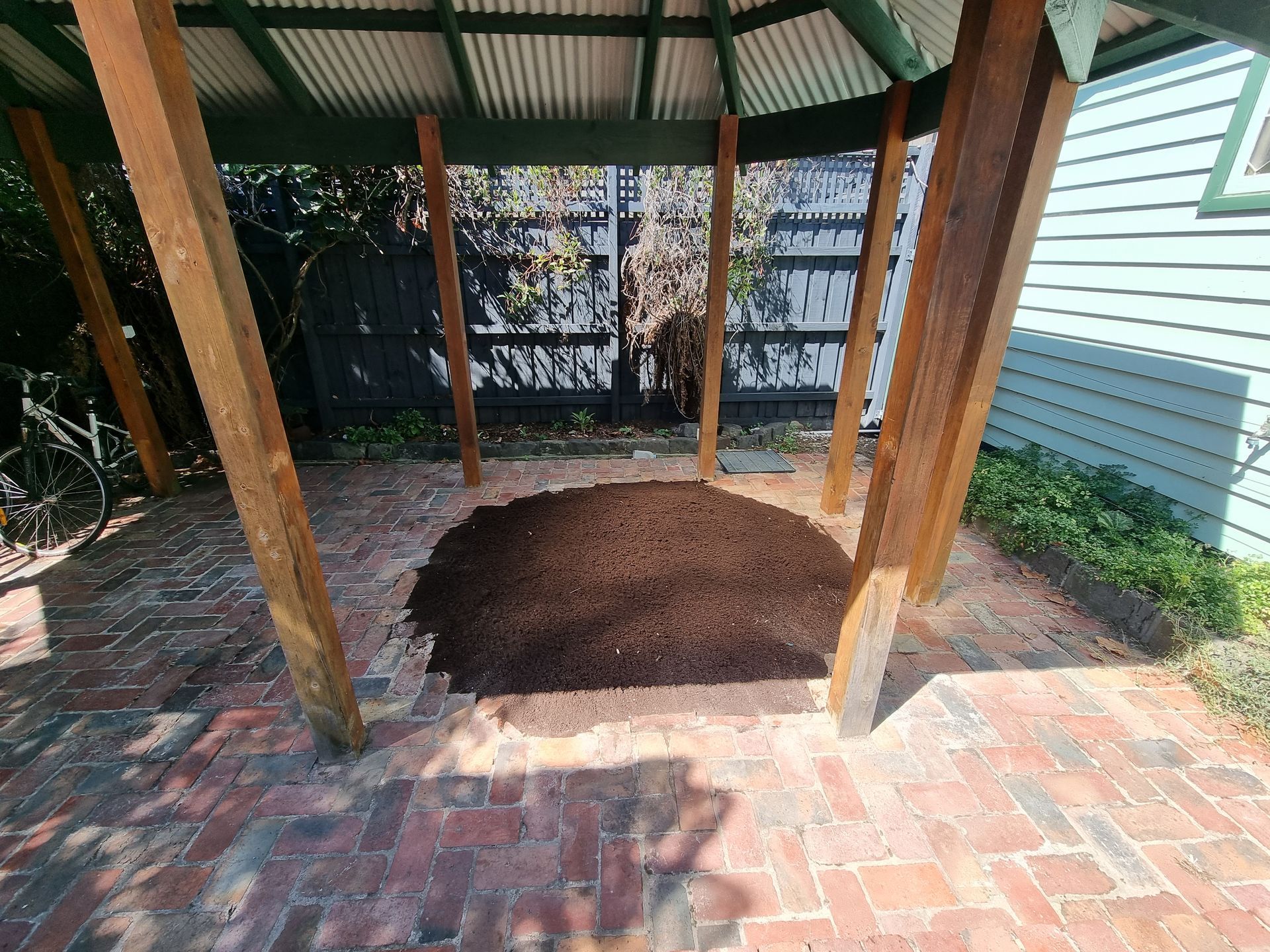 A pile of dark mulch sits in the center of a brick-paved gazebo with wooden support posts  — All Over Pool Removals in Chadstone, VIC