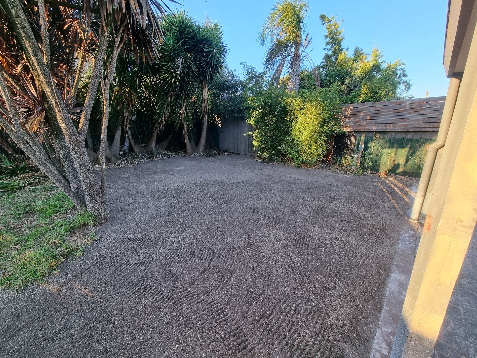 A freshly leveled, gravel-covered area adjacent to a house wall and a patch of grass with surrounding trees — All Over Pool Removals in Doncaster, VIC