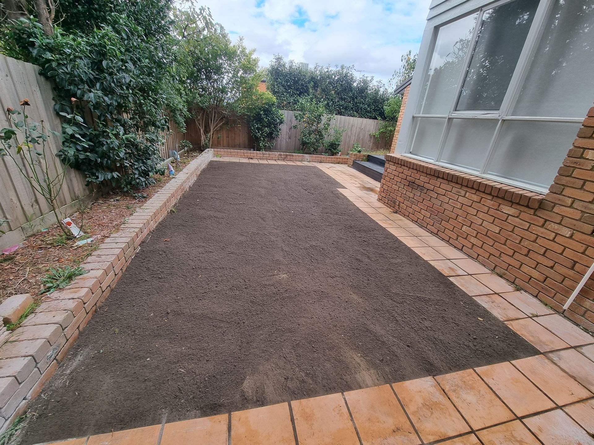 A freshly prepared rectangular garden bed with dark soil, bordered by bricks and tiles in a residential backyard — All Over Pool Removals in Surrey Hills, VIC