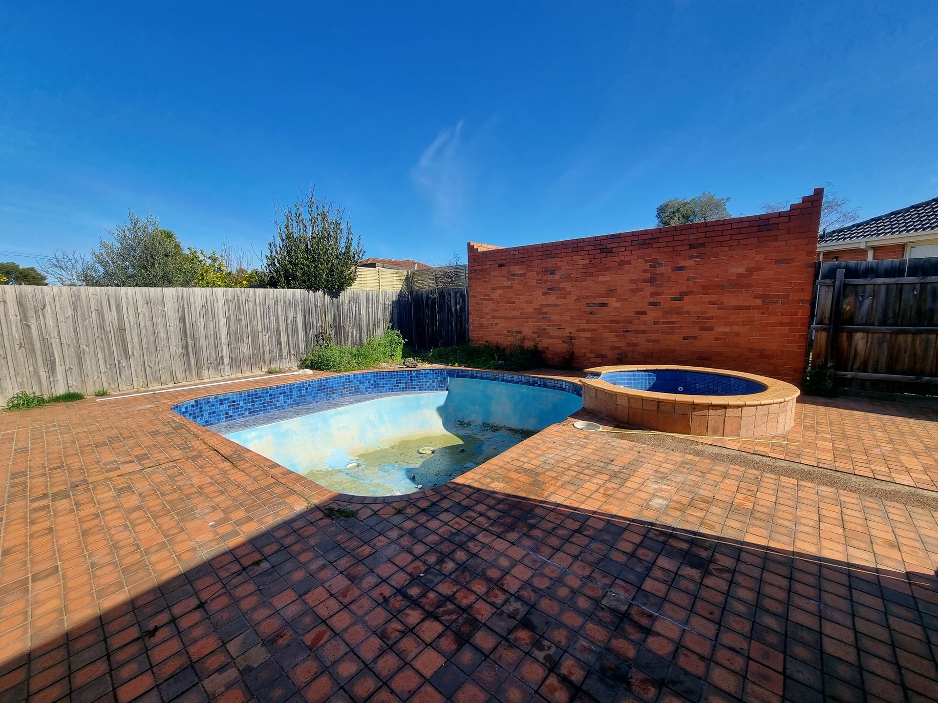 A drained backyard swimming pool and a circular spa on a reddish-brown brick patio under a clear blue sky — All Over Pool Removals in Glen Waverley, VIC