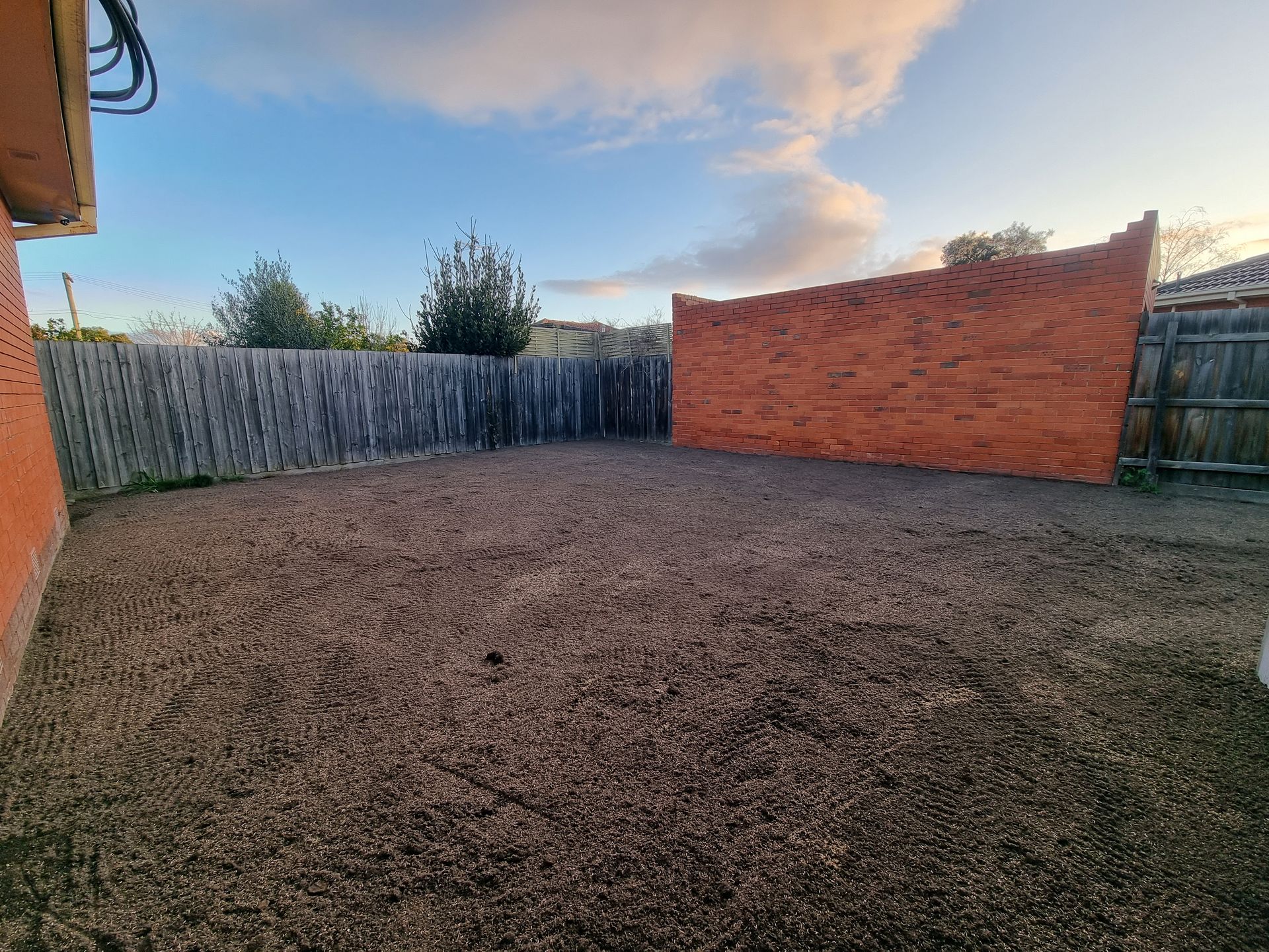 A fenced backyard with a ground-level gravel surface and a decorative reddish-brown stone wall under a clear blue sky  — All Over Pool Removals in Donvale, VIC