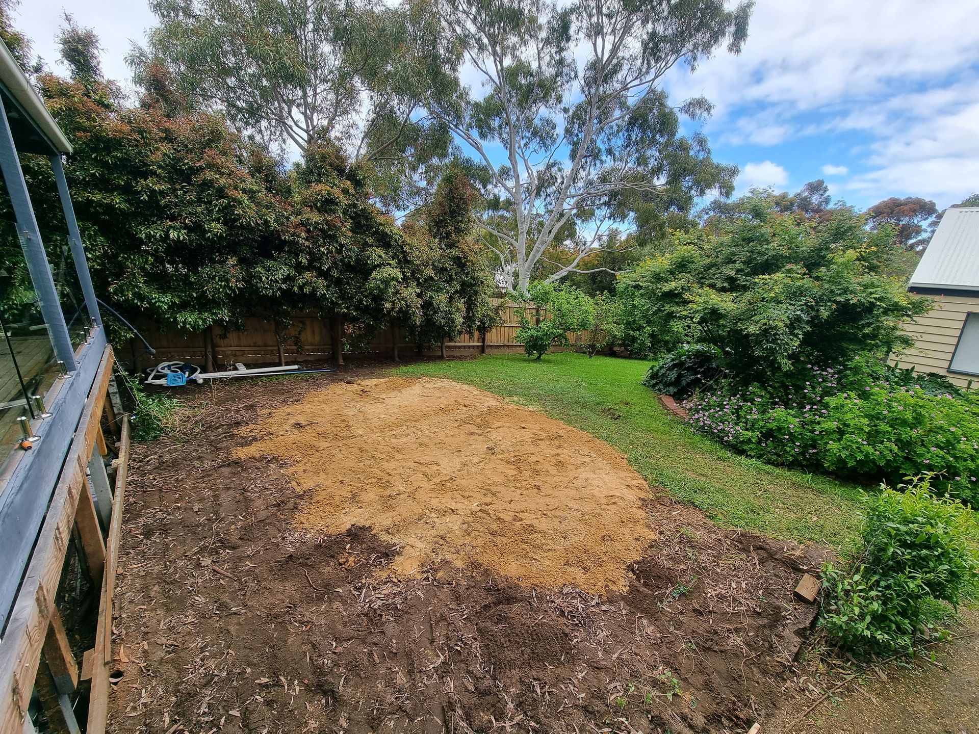 A backyard with a large patch of light-colored wood chips in the foreground, surrounded by garden beds and trees  — All Over Pool Removals in Donvale, VIC