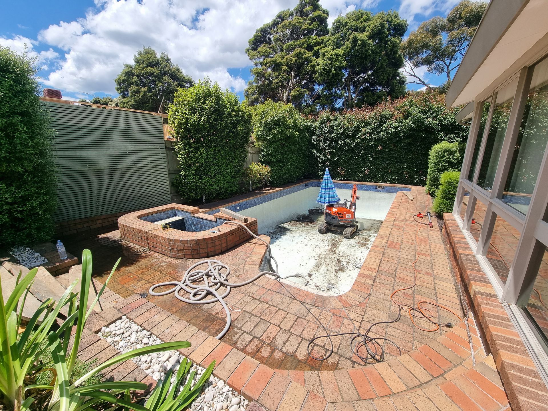 A backyard swimming pool undergoing renovation with construction equipment inside, surrounded by brick paving and greenery  — All Over Pool Removals in Donvale, VIC