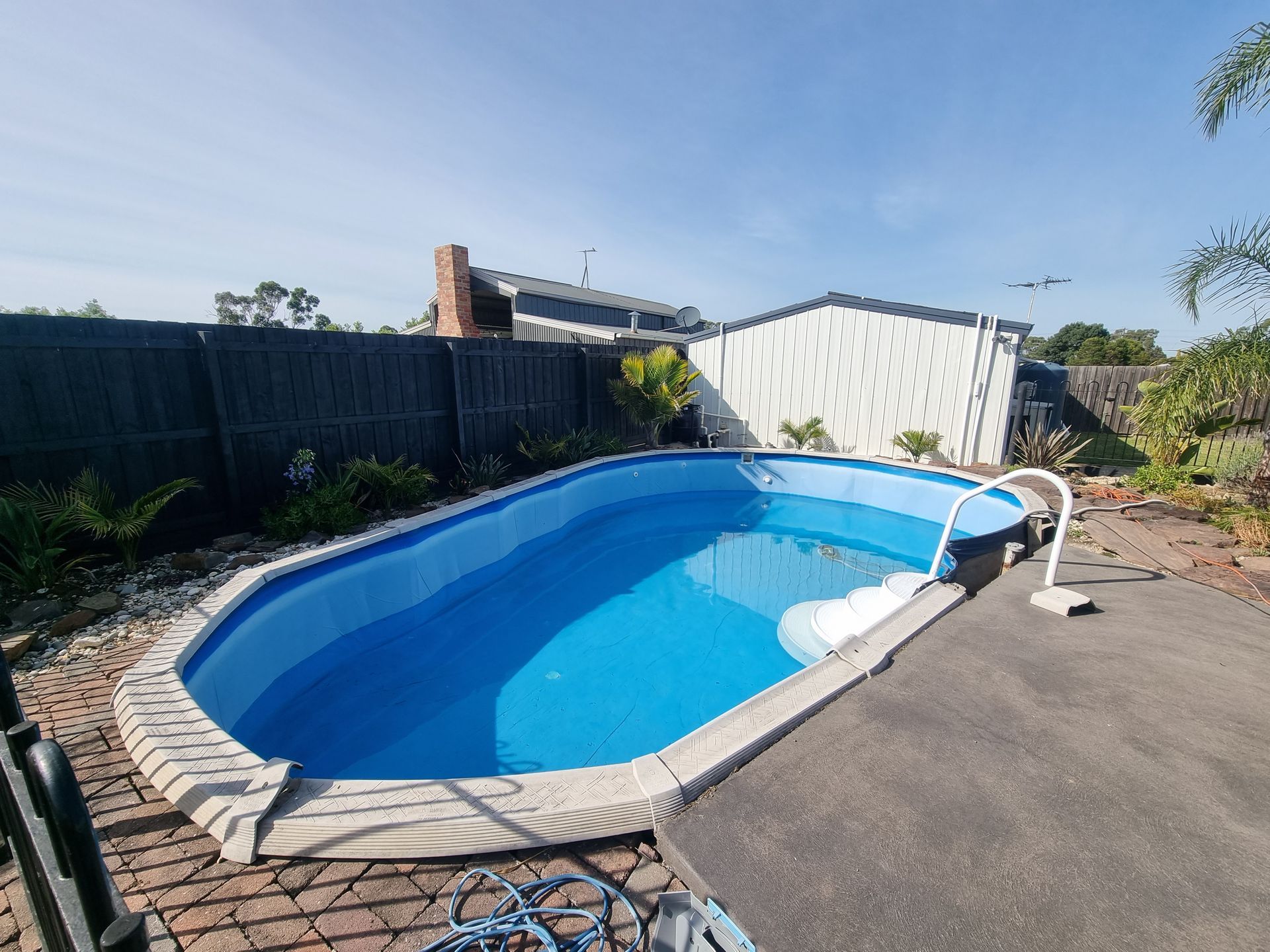 An oval above-ground swimming pool with blue water, surrounded by brick paving and a dark fence in a residential yard — All Over Pool Removals in Chadstone, VIC
