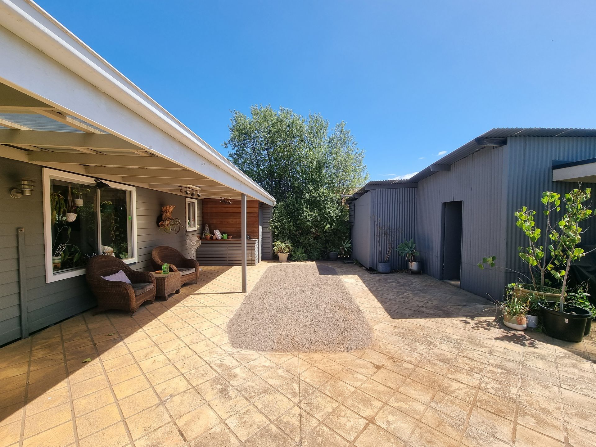 A patio with tiled flooring and a covered seating area next to a gray building under a clear blue sky — All Over Pool Removals in Donvale, VIC
