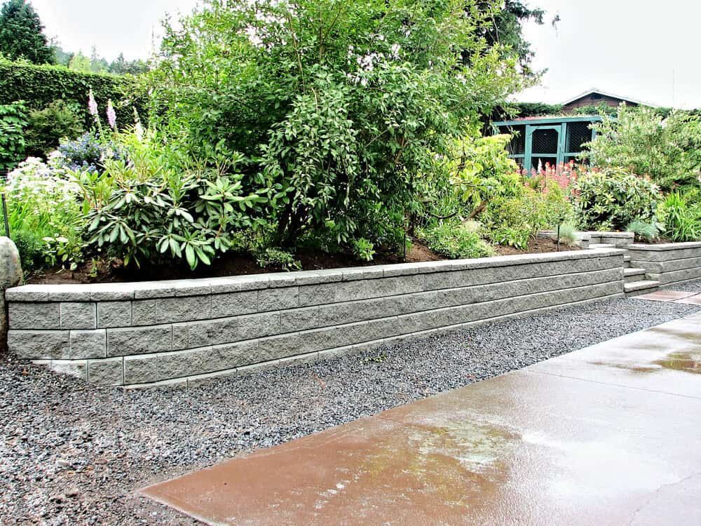 Retaining Wall of Grey Blocks, Gravel Ground, With Green Foliage Behind — All Over Pool Removals in Lilydale, VIC