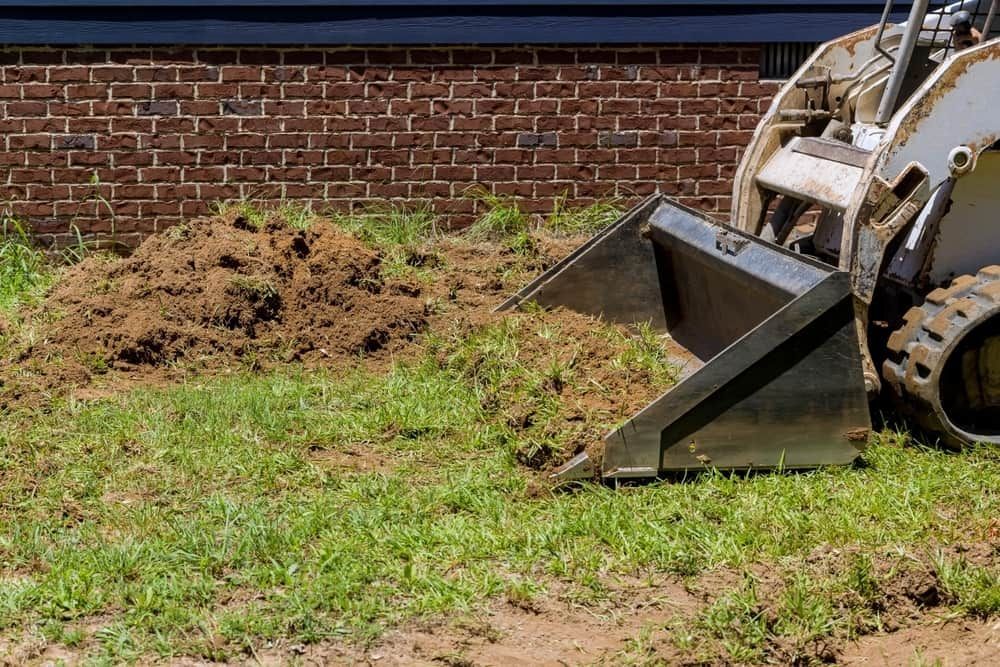 Skid Steer Bucket Scoops Soil and Grass Near a Brick Building — All Over Pool Removals in Doncaster, VIC