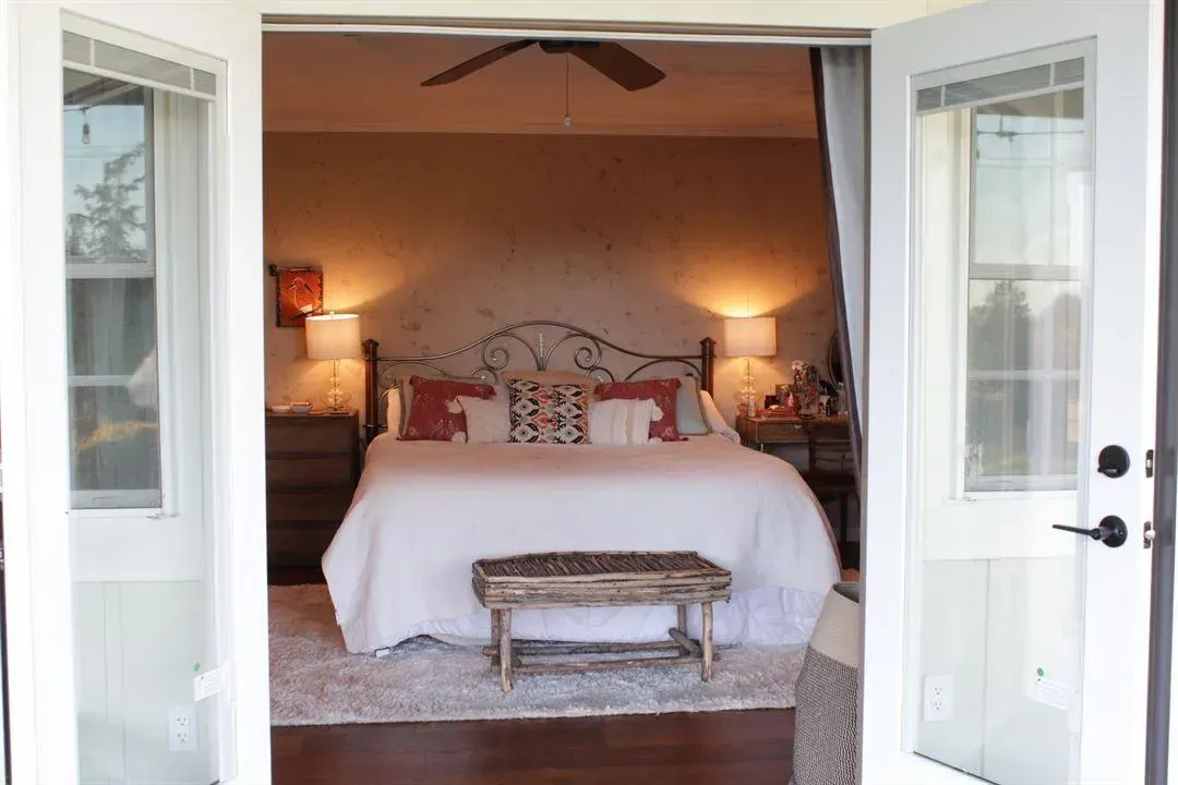 Bedroom interior visible through open double doors; white bedding, bench, bedside lamps.