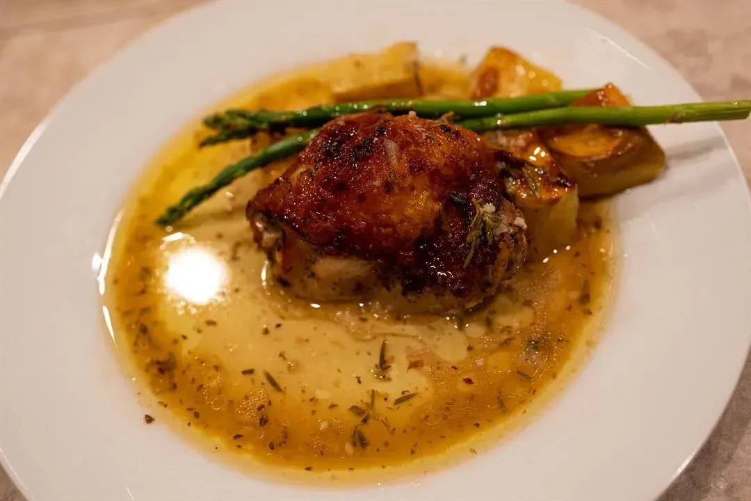 Chicken dish with roasted potatoes, asparagus, and sauce on a white plate.