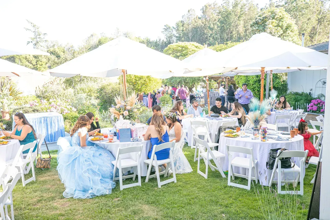 Outdoor event with people seated at tables under white umbrellas.