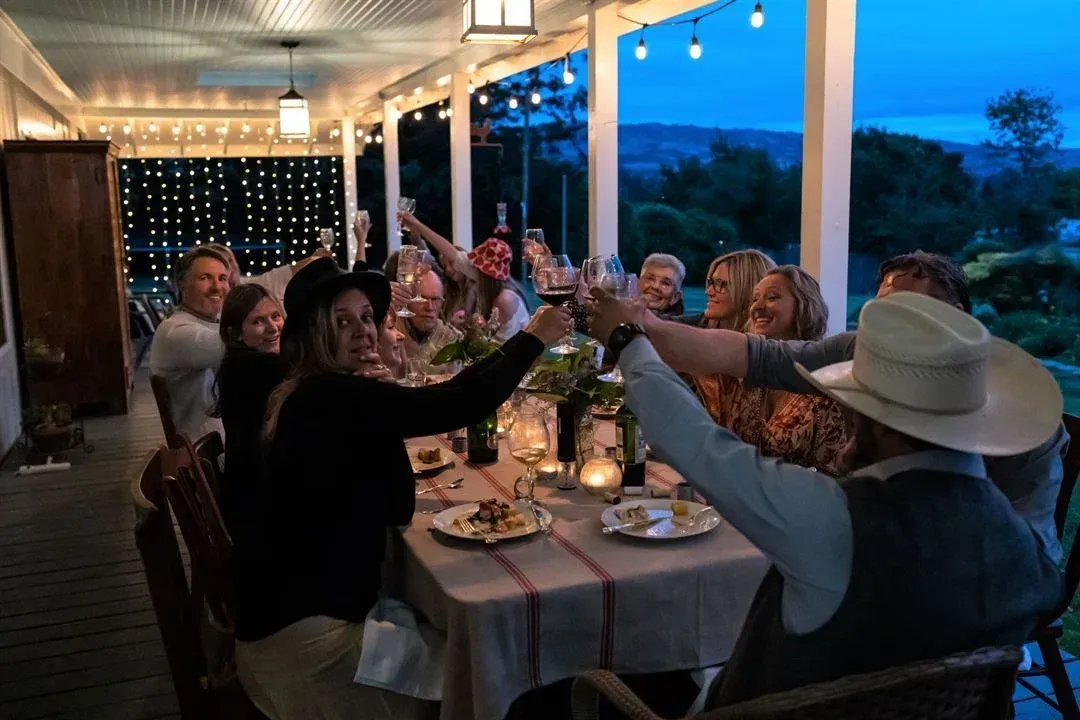 Group raises glasses for a toast at a table on a porch at dusk.