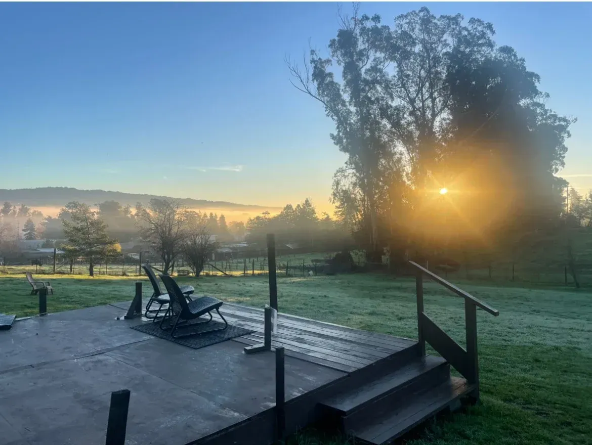 Morning sun over a misty rural landscape, seen from a patio with chairs and steps.