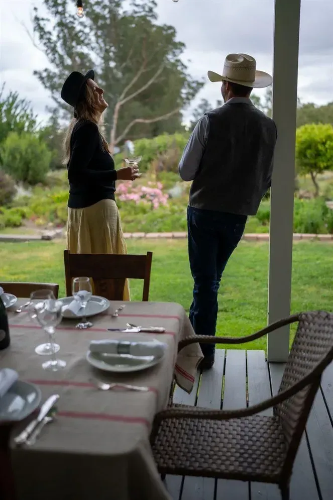 Couple on a porch, looking upwards. Dining table set for meal, overlooking a garden.