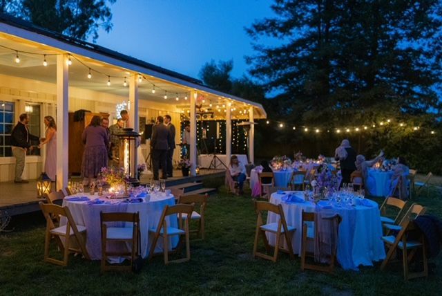 Outdoor evening reception with string lights, tables set for dinner, and people socializing.
