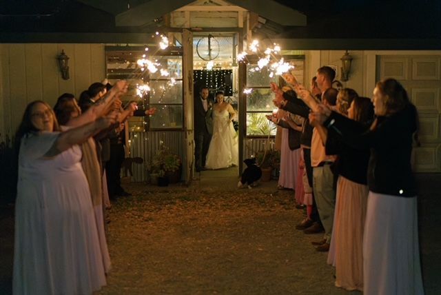 Wedding guests holding sparklers, couple exiting building.