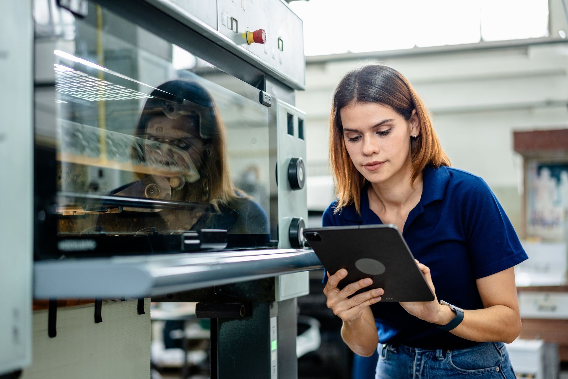 A worker next to a machine in a digital printing factory uses a tablet for monitoring production.